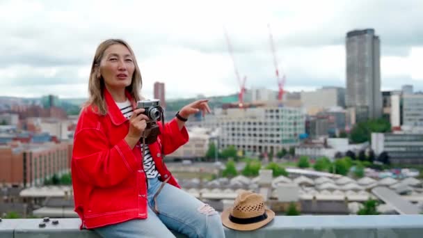 シェフィールドの街の前に座って素晴らしい夏の日に写真を撮る赤いジャケットの幸せなアジアの女性 — ストック動画