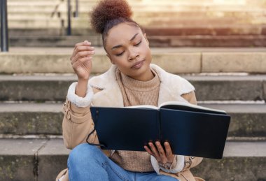 Kadın öğrenci e-öğrenim uzaklık eğitim kursu. Şehirdeki merdivenlerde çalışıyor. Çevrimiçi eğitimi izleyen Afrikalı Etnik Kadın dizüstü bilgisayar kullanıyor.