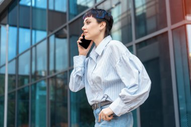 Mavi gömlekli bir kadın arka planda cep telefonu ve iş merkezi kullanıyor.