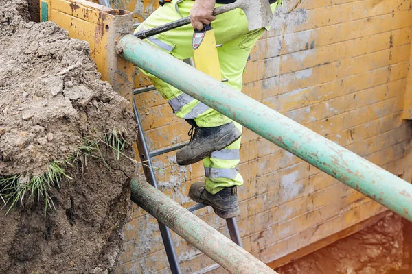 stock image Groundworker builder using steps ladder to get out of the deep drainage eaxcavation trench support box. Builder going up using ladder. Safe workplace fall prevention concept
