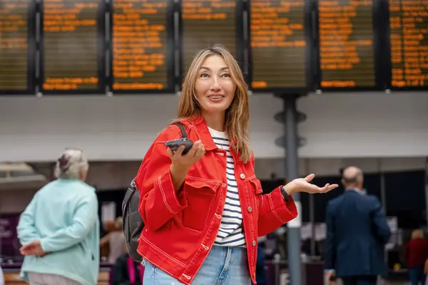 confused asian woman with backpack and holding smartphone while at the train station and the train is arriving., Enjoying travel concept