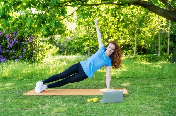 redhead woman teaching, coaching, doing yoga exercise online outdoor in a park Fitness, sport, healthy in any place and time lifestyle concept