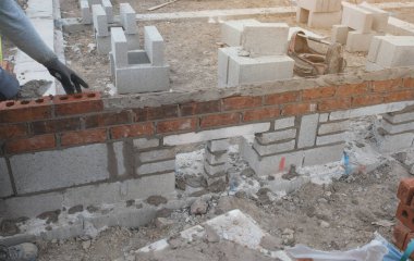 İnşaat alanındaki çimento karışımına tuğla döşeyen duvarcı. Daha ekonomik konut kavramları inşa ederek konut krizini azaltmak