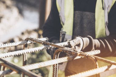 Bir işçi demir çubukları birbirine bağlamak için çelik teller kullanır. Güçlendirilmiş beton yapılar. Beton kiriş için çelik bir kafes yapıyorlar.