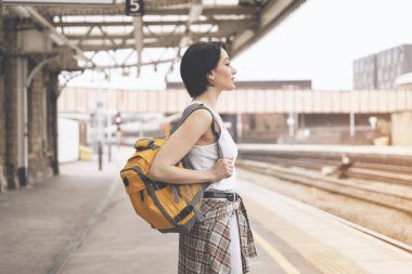 Sırt çantalı kadın tren istasyonunda ve tren geliyor. Seyahat kavramının tadını çıkar