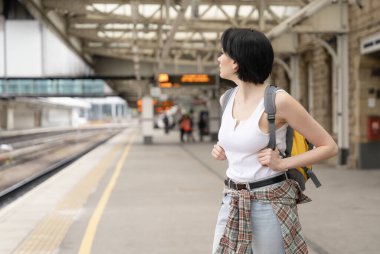 Sırt çantalı kadın tren istasyonunda ve tren geliyor. Seyahat kavramının tadını çıkar