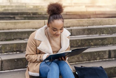 Güzel, Afro-Amerikan bir kız öğrencinin portresi şehrin basamaklarında oturmuş ders çalışma planları yapıyor.