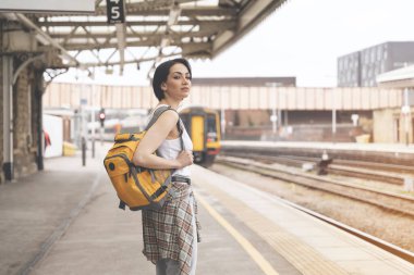 Sırt çantalı kadın tren istasyonunda ve tren geliyor. Seyahat kavramının tadını çıkar