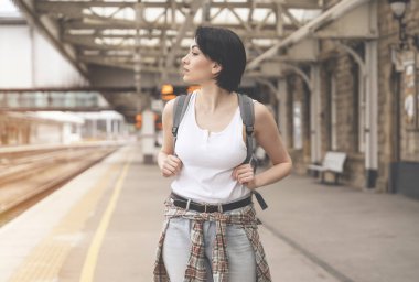 Sırt çantalı kadın tren istasyonunda ve tren geliyor. Seyahat kavramının tadını çıkar