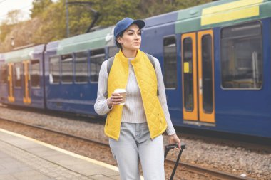 Elinde bavul ve kahve olan kadın tramvayda bekliyor. Keyifli yolculuklar.