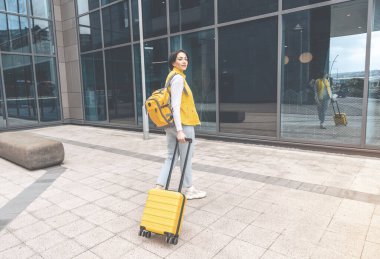 Sırt çantası ve bavulu olan harika bir genç kadın. Tatilde eğlenen kadın. Hafta sonu yurtdışına seyahat eden yolcuların uçuş konsepti