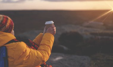 İngiltere 'deki ulusal parkın dağ manzarasında bir fincan sıcak kahveyle serinletici soğuk kış gündoğumunun tadını çıkaran bir kadın. Sırt çantasıyla dağlara yürüyüş. Etkin yaşam konsepti