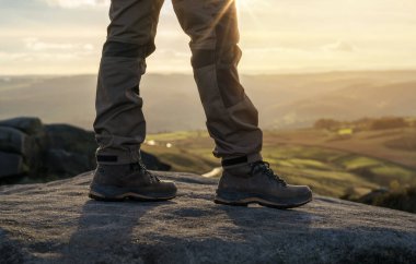 Özel botlu bir adam dağlarda yürüyor. Varış noktasına ulaşıyor ve sonbahar günbatımında Peak District 'teki dağın tepesinde seyahat yaşam tarzı konsepti var.