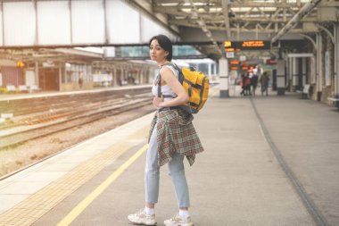 Sırt çantalı kadın tren istasyonunda ve tren geliyor. Seyahat kavramının tadını çıkar