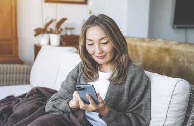 Asyalı kadın evde kahve, sıcak çikolata ve çay içerek, müzik dinleyerek ve aileyle iletişim kurarak harika zaman geçiriyor. Yaşam tarzı kavramı