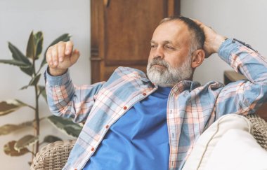 Gülümseyen yaşlı, olgun bir adam gülüyor kitap okuyor, dinleniyor, oturma odasında kanepede oturuyor.