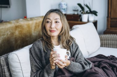 Asyalı kadın evde harika zaman geçiriyor kahve içiyor, sıcak çikolata içiyor, çay içiyor, müzik dinliyor, ailesiyle iletişim kuruyor. Yaşam tarzı kavramı