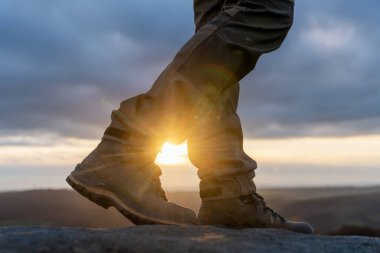 Özel botlu bir adam dağlarda yürüyor. Varış noktasına ulaşıyor ve sonbahar günbatımında Peak District 'teki dağın tepesinde seyahat yaşam tarzı konsepti var.
