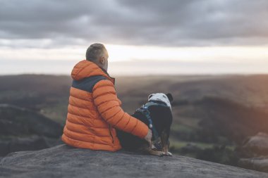 Yaşlı olgun bir adam köpeğiyle dağlarda yürüyüş yapıyor, sağlık, sağlıklı yaşam tarzı ve gülümseme için egzersiz yapıyor. Elinde buldogla oturmuş sakin bir günün tadını çıkaran yaşlı bir beyefendinin yüzü.
