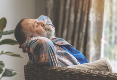 Yaşlı, yaşlı bir adam gülüyor kitap okuyor, dinleniyor, oturma odasında kanepede oturuyor.