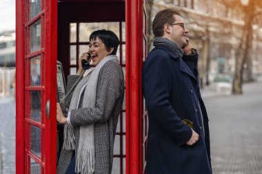 Yakışıklı bir adam ve güzel bir kadın şehirde yürürken birbirlerine sarılıyorlar, eğleniyorlar, kırmızı telefon kulübesinden arıyorlar, yaşam tarzı fotoğrafı.