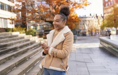 Elinde bir fincan kahve tutan neşeli bir kadın. Süveter giyen, arkadaşlarıyla buluşan, gülümseyen, kıvırcık esmer bir kadın.