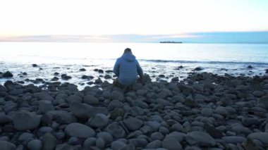 Deniz kenarında tek başına dinlenen ve soğuk kış günü gün batımında telefonda zaman ayarlı konuşan bir adam. Seyahat yaşam tarzı konsepti