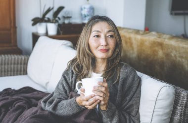 Asyalı kadın evde harika zaman geçiriyor kahve içiyor, sıcak çikolata içiyor, çay içiyor, müzik dinliyor, ailesiyle iletişim kuruyor. Yaşam tarzı kavramı