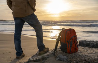 Sırt çantalı sakallı adam gün batımında sıcak güneşli bir günde deniz kenarında tek başına dinleniyor. Seyahat yaşam tarzı konsepti