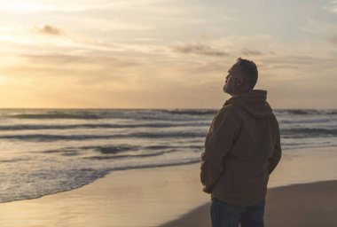 Sırt çantalı sakallı adam gün batımında sıcak güneşli bir günde deniz kenarında tek başına dinleniyor. Seyahat yaşam tarzı konsepti