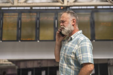 Tren istasyonundayken elinde akıllı telefon tutan sinirli bir adam ve tren geliyor, seyahat konsepti.