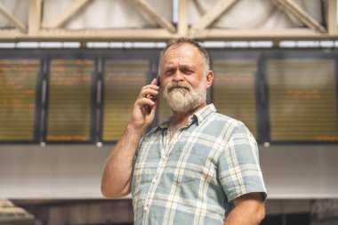 Tren istasyonundayken elinde akıllı telefon tutan sinirli bir adam ve tren geliyor, seyahat konsepti.