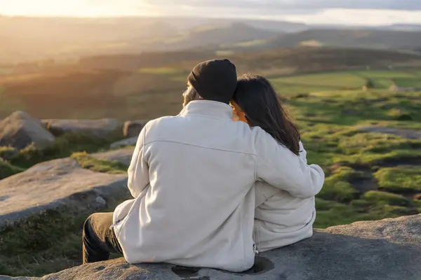 Back view of the happy couple in love sitting on top of a mountain enjoying a sunset landscape view  success life concept breath passion wisdom wellbeing