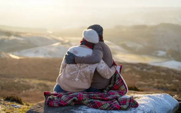 Back view of the happy couple in love sitting on top of a mountain enjoying a sunset winter landscape view  success life concept breath passion wisdom wellbeing