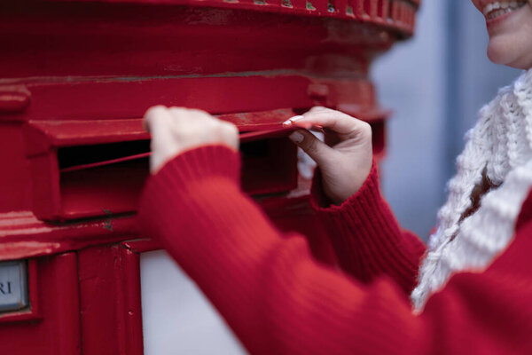 woman in a coat and white hat  putting a card in the red postbox and walking around an English city on a snowy day