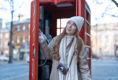 Outdoor portrait of woman using camera   against red phonebox in English city