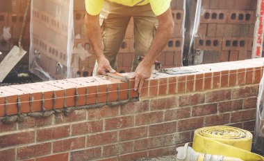 Industrial bricklayer laying bricks on cement mix on construction site