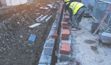 Hard working bricklayer laying concrete blocks on top of concrete foundation on new residential housing site. Fight housing crisis by building more affordable houses concept