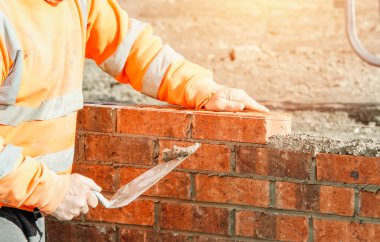 Close up of industrial bricklayer laying bricks on cement mix on construction site