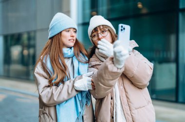 Gülümseyen genç bayan kız arkadaşlar birlikte eğleniyorlar, konuşuyorlar ve şehir dışında cep telefonları kullanıyorlar. İnsanlar, iletişim, arkadaşlık ve yaşam tarzı kavramı