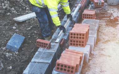 Hard working bricklayer laying concrete blocks on top of concrete foundation on new residential housing site. Fight housing crisis by building more affordable houses concept