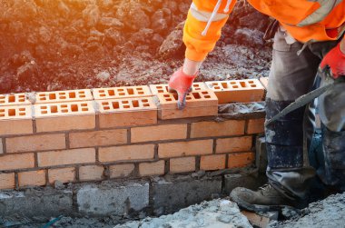 Industrial bricklayer laying bricks on cement mix on construction site. Fighting housing crisis by building more affordable houses concept