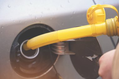 A man filling fuel tank of his car with diesel fuel from the jerry can as there is no fuel at the petrol station, close up clipart