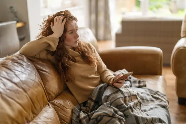 A Beautiful redhead woman watching TV sitting on a sofa at home, watching TV on the couch at home in the living room