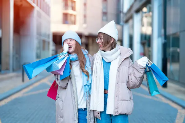 women girlfriends   with colorful shopping gift bags having a fun time together, talking and using phones  outdoor in urban city. people, communication, friendship, shopping and lifestyle concepts