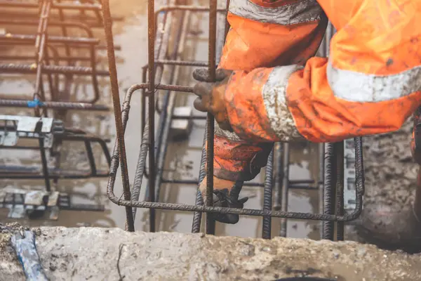 Bir işçi demir çubukları birbirine bağlamak için çelik teller kullanır. Güçlendirilmiş beton yapılar. Beton kiriş için çelik bir kafes yapıyorlar.