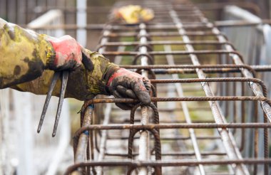Bir işçi demir çubukları birbirine bağlamak için çelik teller kullanır. Güçlendirilmiş beton yapılar. Beton kiriş için çelik bir kafes yapıyorlar.