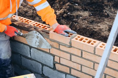 Industrial bricklayer laying bricks on cement mix on construction site. Fighting housing crisis by building more affordable houses concept
