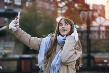 Mutlu genç bir kadın eğleniyor, telefon kullanıyor, müzik dinliyor ve şehirde dans ediyor. İnsanlar, iletişim, alışveriş ve yaşam tarzı kavramı