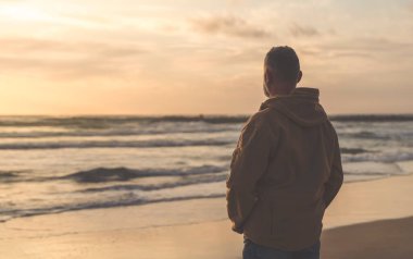 Sırt çantalı sakallı adam gün batımında sıcak güneşli bir günde deniz kenarında tek başına dinleniyor. Tonlanmış görüntü. Seyahat yaşam tarzı konsepti